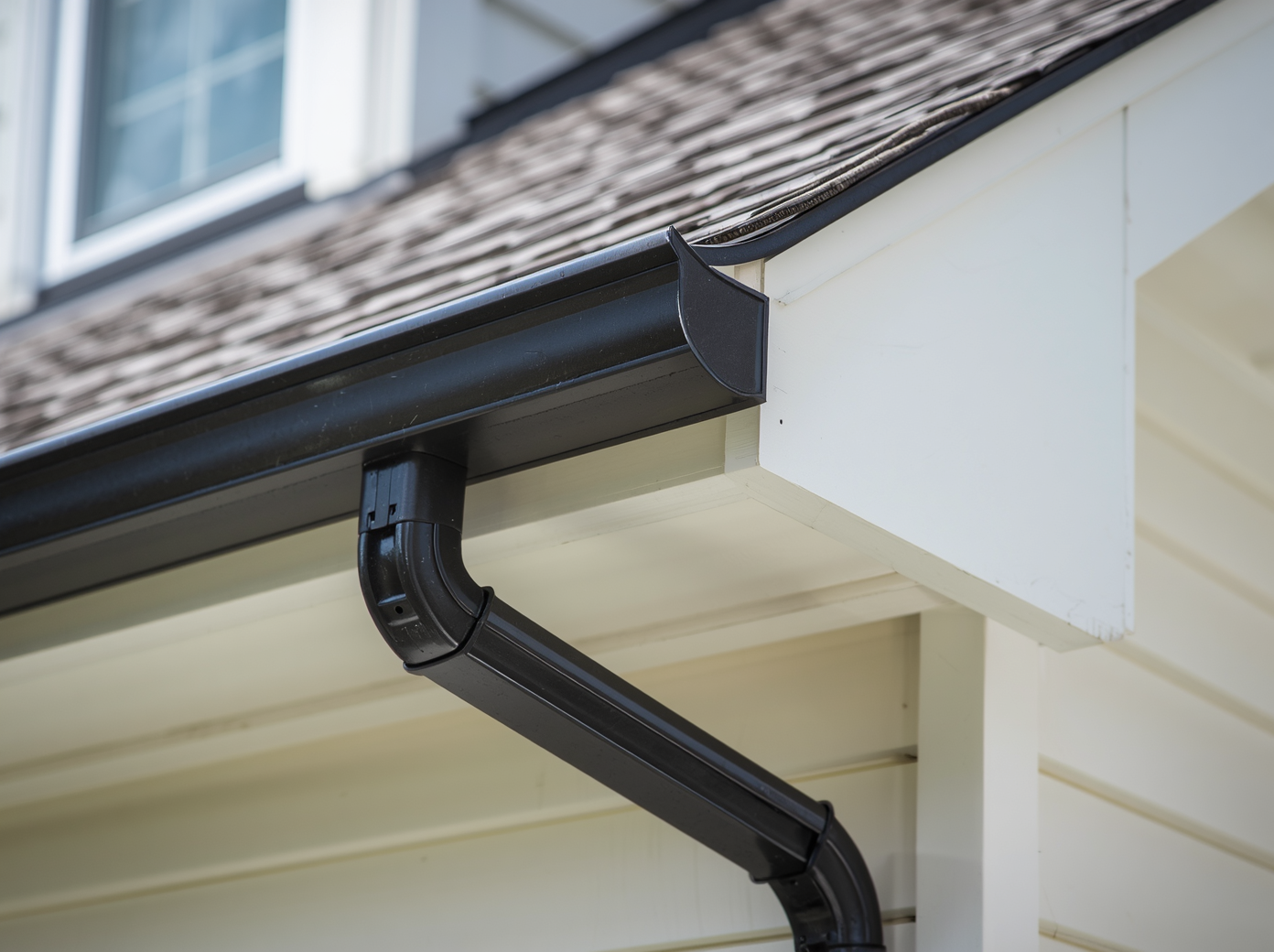 Close-up view of a dark-colored K-style gutter properly mounted on white fascia board